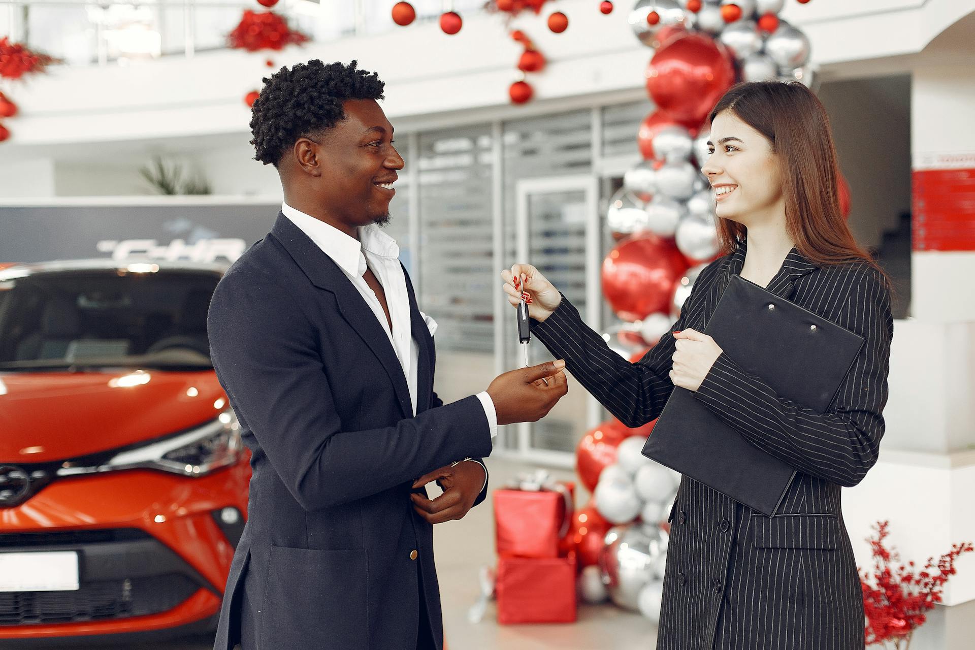 Car dealer handing a set of keys to a smiling customer beside a new vehicle